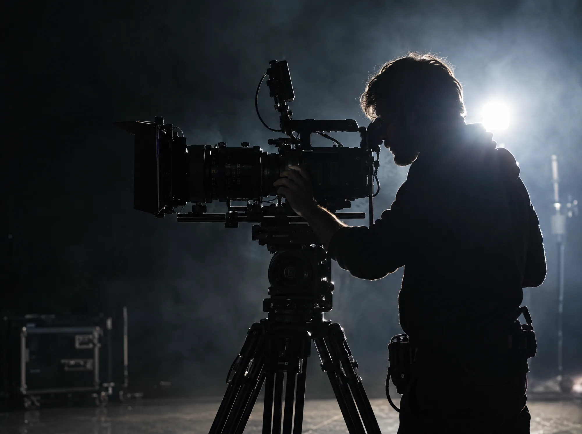 A camera operator silhouetted behind a cinema camera in a beam of light