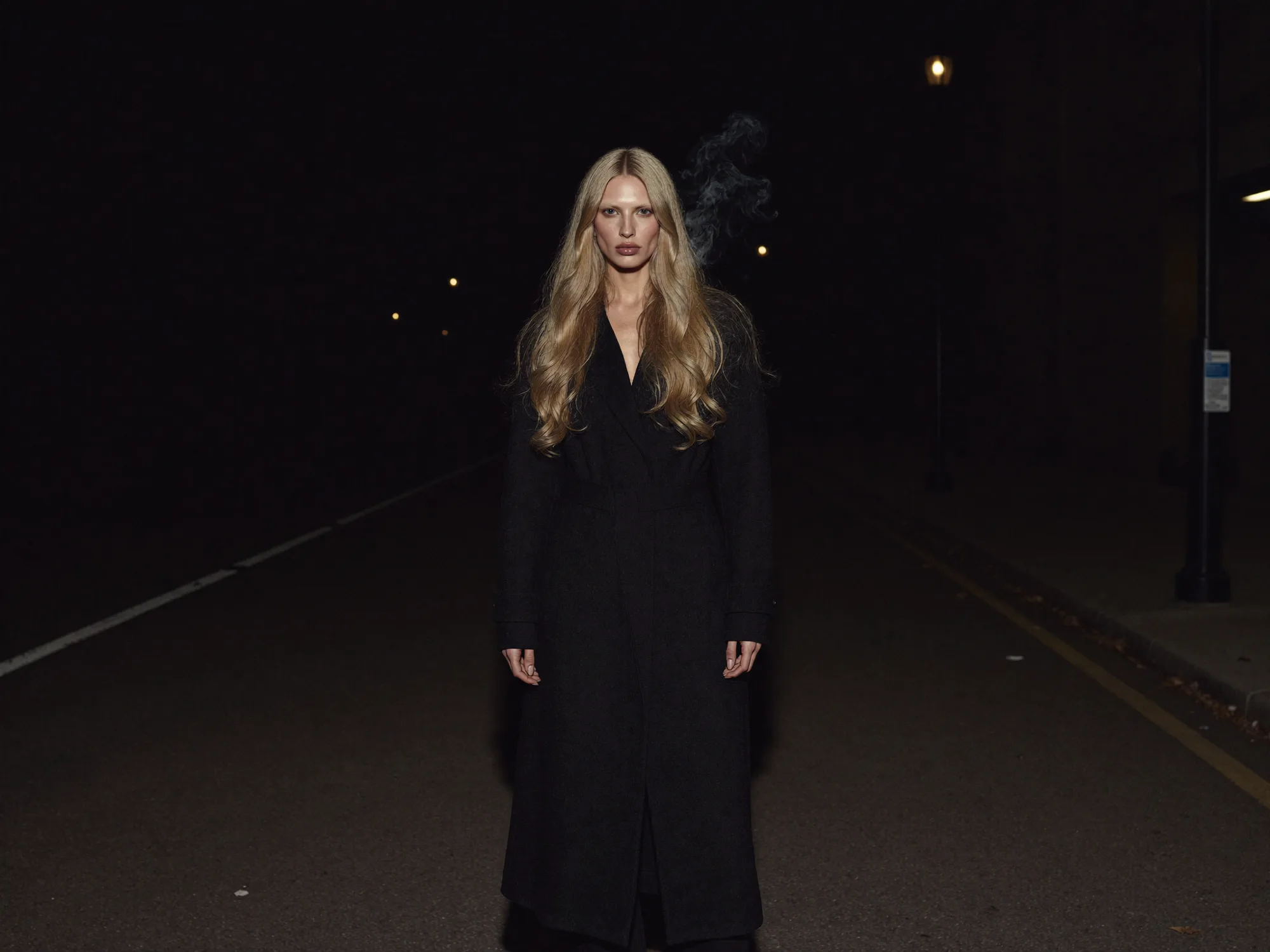 A woman in black standing alone on an empty road at night