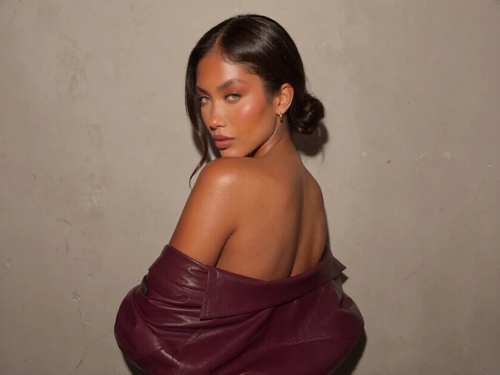 A woman in a brown leather off shoulder wrap against a warm plaster wall
